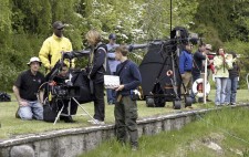 A dozen crew line up on a grassy lake bank, looking out to the action beyond the frame.