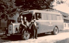 An archive photograph shows an old-fashioned bus, its windows blacked out, a Nazi eagle on the side. Three men pose for the photograph: one sits on the high wheel arch, another leans against it, a third leans out from the front passenger window.