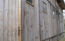 The outside of the garage, built from planks of wood, with three sets of double doors doors, each with high window panels.