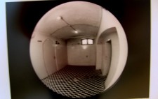 An archive photograph shows a round fisheye mirror which reflects the white tiles and black and white floor of the empty chamber
