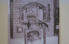 Photograph showing a large photographic reproduction placed against a wall showing an old-fashioned brick bread oven, it doors open.