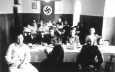 An archive photograph showing a wood panelled dining room, long tables covered in white cloths. Around twenty staff members sit, turned to the camera, wearing a mixture of white coats, civilian clothes and uniforms.