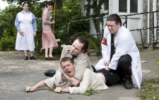 Inmate Otto is sprawled on the ground outside the institution, an orderly pinning him down in a necklock. A second orderly in white coat and red Nazi armband kneels down. In the background the nurse and Elise watch helplessly.