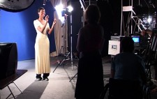 In a studio, Sherrie stands in front of a bluescreen backdrop, lit by strong film lights. A TV monitor faces her, playing the film, so she can time her delivery to the film.