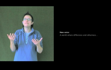 A woman faces camera, communicating in sign language and filmed against greenscreen. To her left is captions text, white on black, reading 'New voice: A world where difference and otherness...'