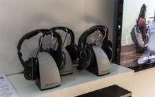 Three cordless headsets on a white shelf, next to a TV showing the film Reflections from the Bed.