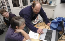 During the shoot, Bryan Panks and Liz Crow, with photographer Matt Bigwood looking on, look intently at a computer laptop.