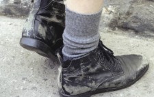 A close-up of a pair of feet in some scruffy black shoes and grey ankle socks.