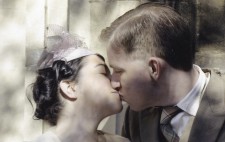 Outside a church, Gloria, clothed in a ivory wedding dress, holding a spray of lilies and ivy, and Walter, dressed in a brown suit, lean in to each other to kiss. 