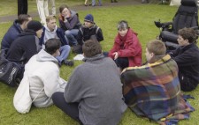 Director Liz Crow sits on the lakeside grass surrounded by the swimming lads and members of the crew