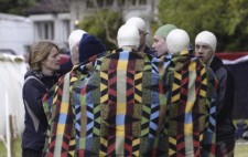 The swimmers stand in a huddle, looking cold and draped head to toe in a large communal blanket.