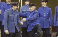 Dressed in royal blue overcoats and military-style caps, five members of the band, one with his leg raised high, share a joke between takes.