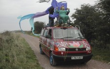 Perched on the red van with its spray painted flora and fauna is the wheelchair occupied by 'Katie'. From the back of the chair billows streams of fabric. Members of the crew kneel on the roof.