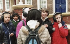 Six primary age children stand at the edge of the Square wearing large earphones, other classmates waiting just behind them to kit up.
