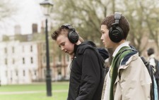 Two primary age school boys wearing large earphones stand in the grassy Square deeply absorbed in the audio.