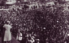 Helen stands on a stage in front of a vast crowd of people, their faces upturned