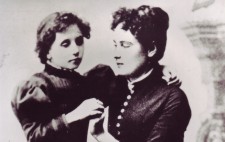 Dressed in late Victorian gowns, Helen, aged about 8, stands next to a seated Annie, in her 20s. Helen drapes an arm around her neck and Annie fingerspells onto her other hand and looks tenderly at her pupil.