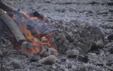 A net of chicken wire encases the figures, while the fire recedes to embers.