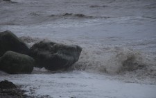 Waves roll towards beach boulders.