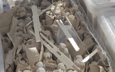 The figures are stacked in rows, each wrapped in paper. They are surrounded by chicken wire, held in place with plastic crates and scattered with pieces of kindling.