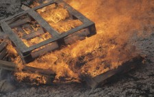 An inferno of orange flame consumes a pile of wooden pallets.