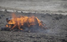 A rough sea, the waves encroaching up the shore. A large bonfire burns furiously.