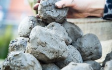 A hand adds another clump to a mound of clay.