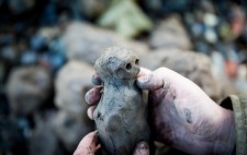 Liz holds a completed figure between her hands. It is rough-hewn, with eyes deep indentations.