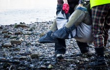 Liz’s legs protrude from the carry sling, the shingle of the foreshore glistening wet beneath her.