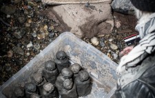 An open plastic crate sits on the foreshore, the figures lined up inside it. Next to it are the hessian-covered blocks Liz leans on to make the figures.