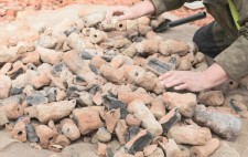 The figures, fired, burned and broken, are piled upon a hessian mat. Liz reaches out towards them.