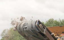 The arm of the machine projects upwards, a black conveyor belt propelling chips and dust into the air.