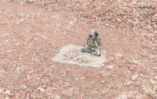 Liz sits in an expanse of crushed bricks, in reds and pinks. In front of her is a hessian mat with the remains of the figures, which echo the colours of the landscape.