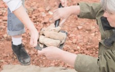 Liz hands over a small black shovel which holds several fired figures, their colour echoing the pinks of the crushed bricks on the ground below.