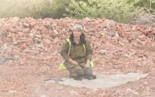 Liz sits, surrounded by bricks, watching the milling as dust drifts across.