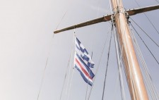 High up on a mast fly two flags: a blue and white checkered flag above one of horizontal stripes in blue, white and red.