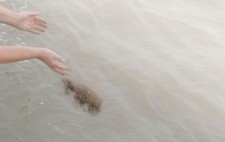 Dust and ground remains fly from outstretched palms held above muddy water.