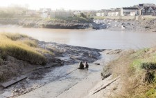 At the bottom of the slipway, with banks of mud giving way to the river beyond, Liz and a member of the production team sit on the ground, gazing out to the water.