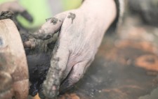 Hands receive the mud as it is extruded from the machine.