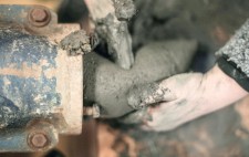 Hands receive the mud as it is extruded from the machine.