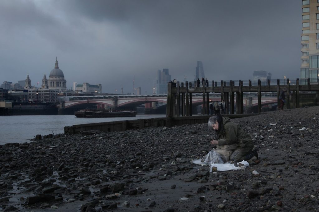 Against a backdrop of St Paul's Cathedral and Blackfriars Bridge, dark clouds rolling in, Liz sculpts the figures, almost merging into the dank shingle foreshore.
