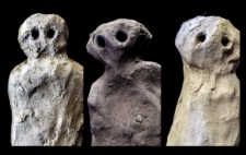 Screen is split vertically into three. In each of the three, is a completed sculpted figure, now dried, rugged and rough hewn, against black backdrop. Palm-sized, each figure is of similar simple, almost abstracted form: rough body shape, minimal features, eyes deep black circles sunk into the head, gazing direct to the viewer.
