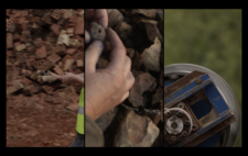 Screen is split vertically into three. Left, a person carries a shovel of the broken figures, against a backdrop of heaped red brick. Centre, hands cradle the burnt remains of a single figure, burnt by the flames. Right, a large machinary wheel, against a backgrop of leafy trees.